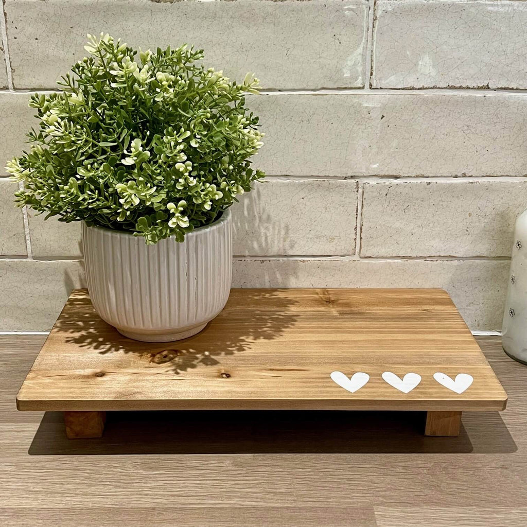 A neutral plant pot sat on a wooden display tray featuring 3 white painted hearts