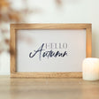 Framed sign with 'Hello Autumn' text on a wooden surface with a blurred background
