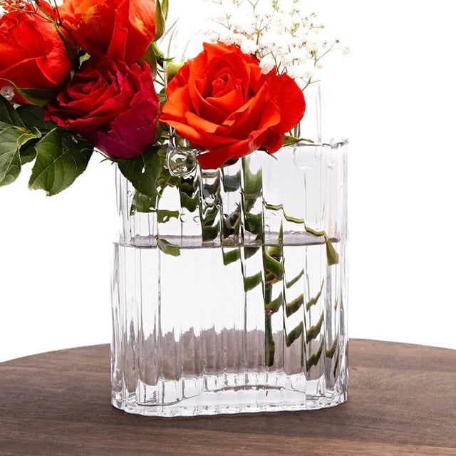 Clear glass handbag vase with red roses on a wooden round tray