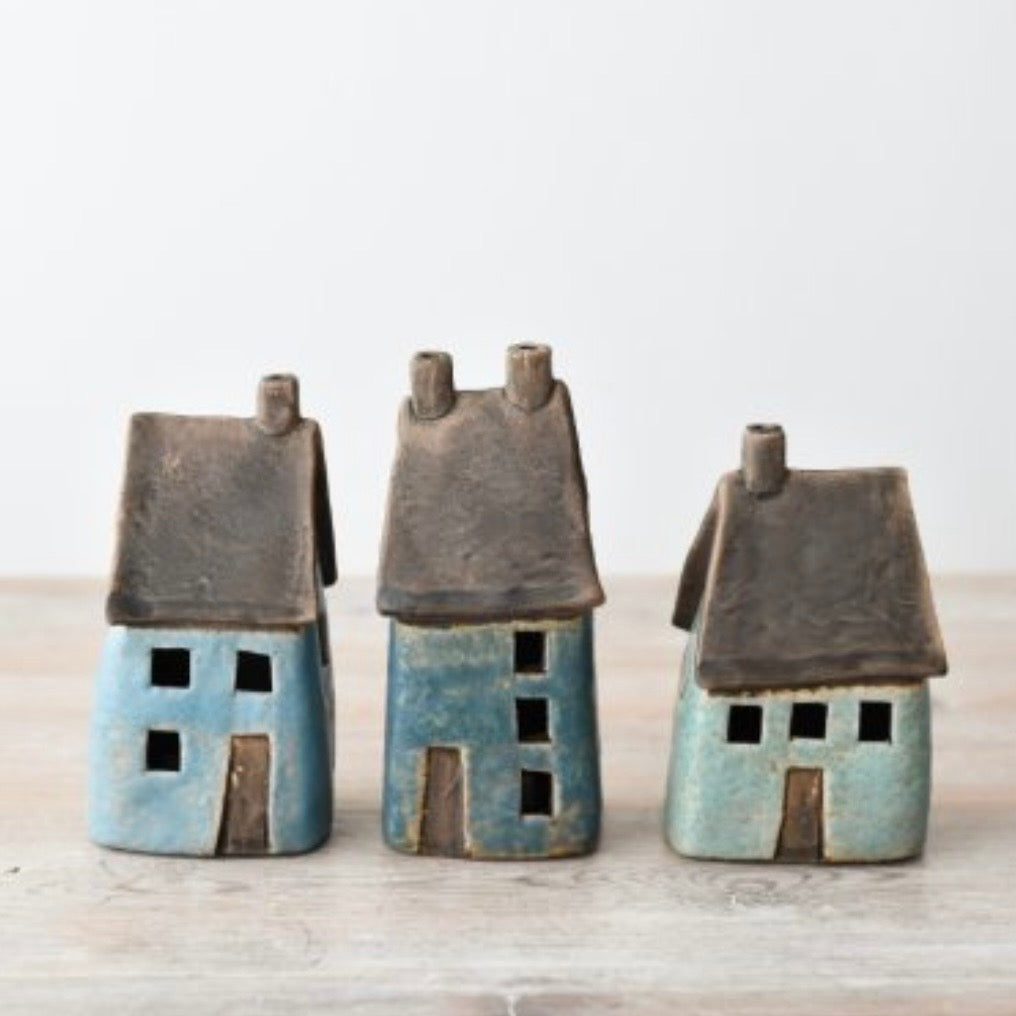 Three small ceramic house figurines in blue and turquoise glazes with dark brown roofs, displayed on a wooden shelf surface