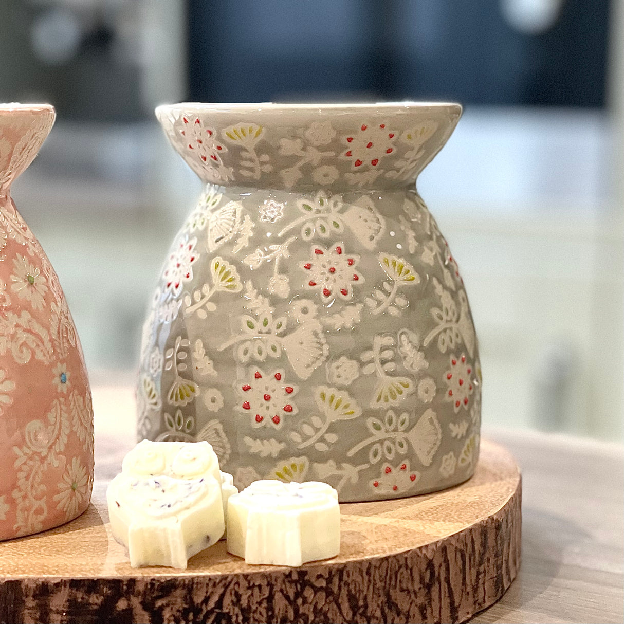Decorative ceramic oil burner with floral patterns on a wooden stand.