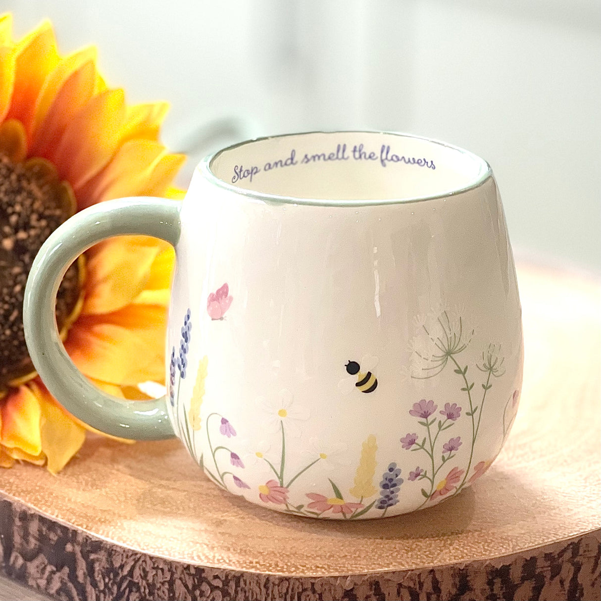 White mug with floral designs and a sunflower on a wooden surface