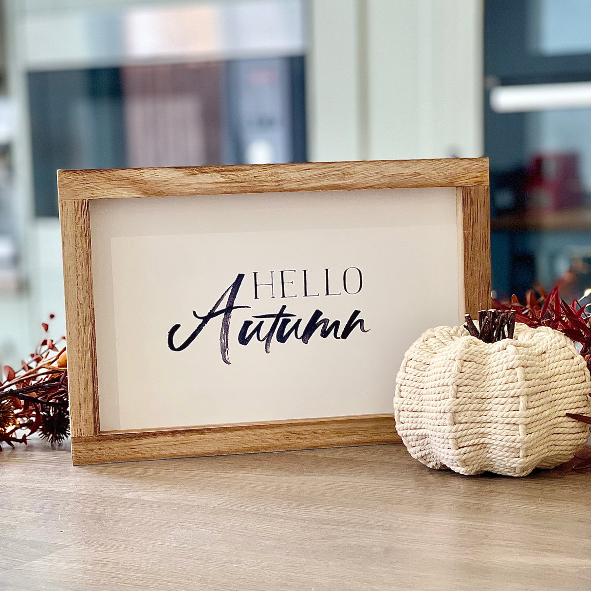 Framed sign with 'Hello Autumn' text on a wooden surface with decorative elements.