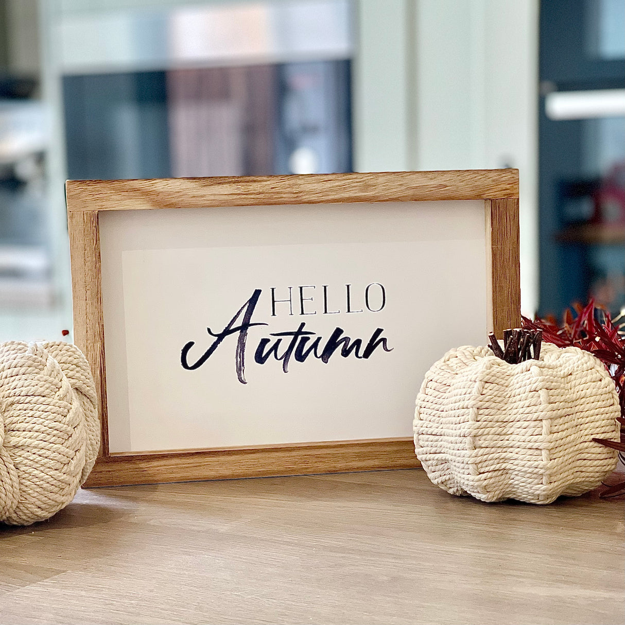 Framed 'Hello Autumn' sign with decorative pumpkins on a wooden surface.