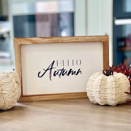 Framed 'Hello Autumn' sign with decorative pumpkins on a wooden surface.