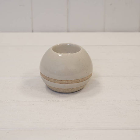 A small round ceramic vase with a glossy off-white finish and a textured beige band around the middle, set on a white wooden surface against a white paneled background.