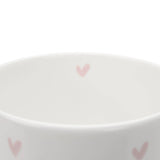 A close up of a white ceramic fine bone china mug with pink heart patterns on a white background