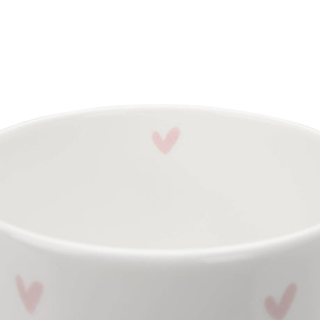 A close up of a white ceramic fine bone china mug with pink heart patterns on a white background