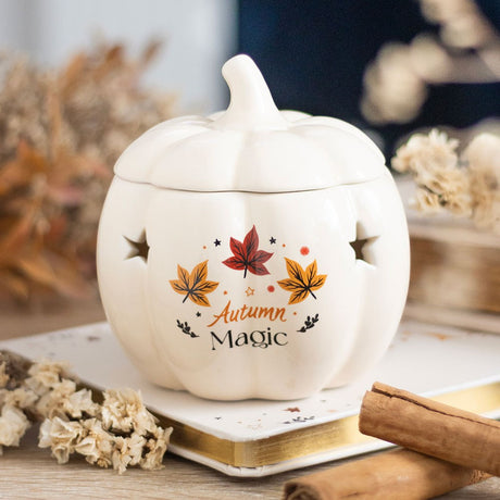 White ceramic pumpkin with 'Autumn Magic' text and leaf designs on a blurred background