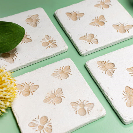 White stone coasters with bee designs on a green background