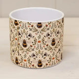 Cylindrical plant pot with bee and floral pattern on a plain background