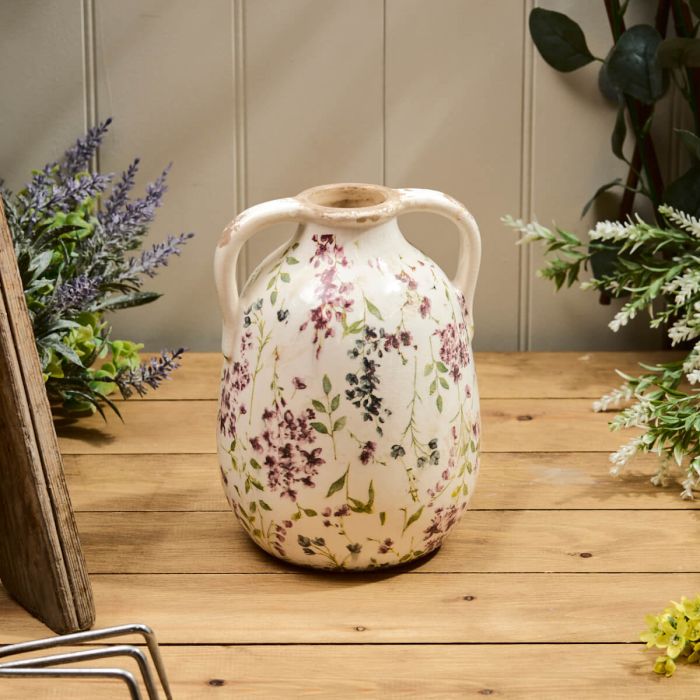 Decorative vase with floral pattern on a wooden surface with plants in the background