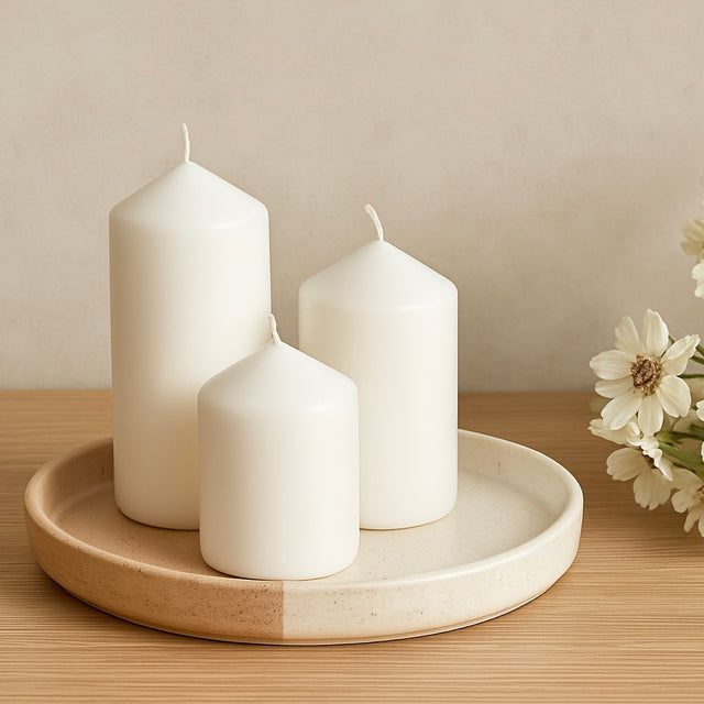 A ceramic Candle Plate with 3 white pillar candles placed pn top. On a wooden table with cream flowers