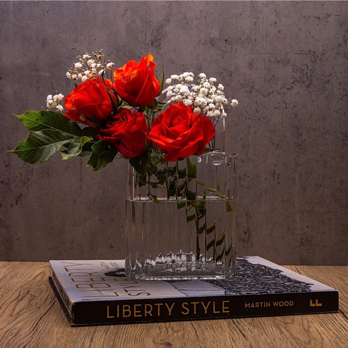 Clear handbag vase with red roses and white flowers on a book titled 'Liberty Style' by Martin Wood.
