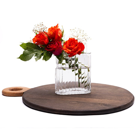 Clear glass handbag vase with red roses on a wooden round tray