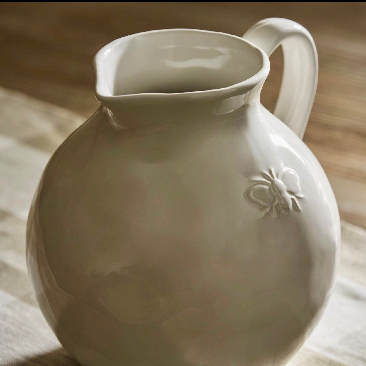 White ceramic pitcher with a subtle bee design on a wooden surface