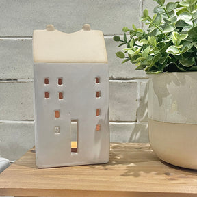 Ceramic house-shaped lantern with a plant on a wooden surface