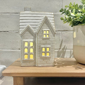Decorative house-shaped lantern with a plant on a wooden surface against a stone wall.