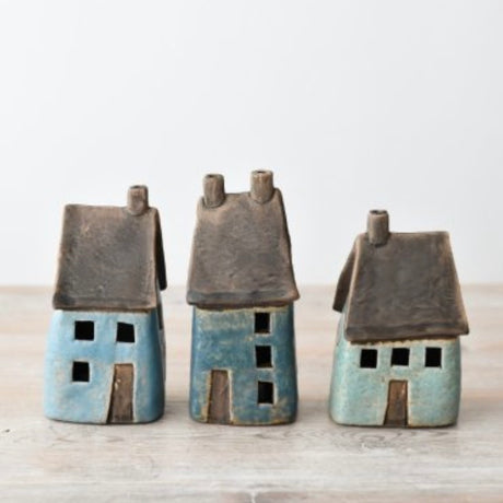 Three small ceramic house figurines in blue and turquoise glazes with dark brown roofs, displayed on a wooden shelf surface