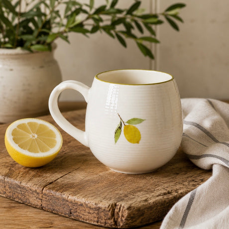 A Sophie Allport cream mug with a lemon design on a wooden surface, accompanied by a striped towel.