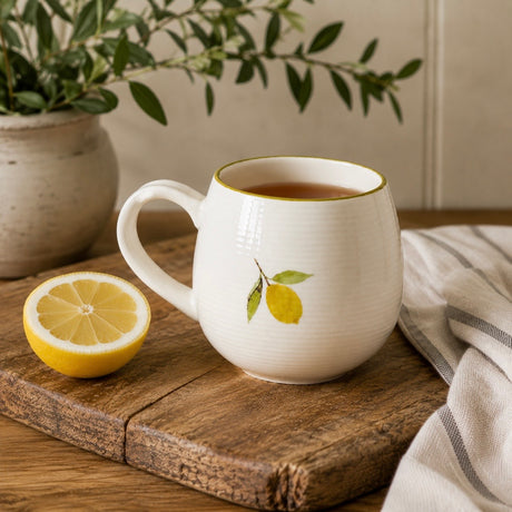A Sophie Allport cream mug with a lemon design on a wooden surface, accompanied by a striped towel.