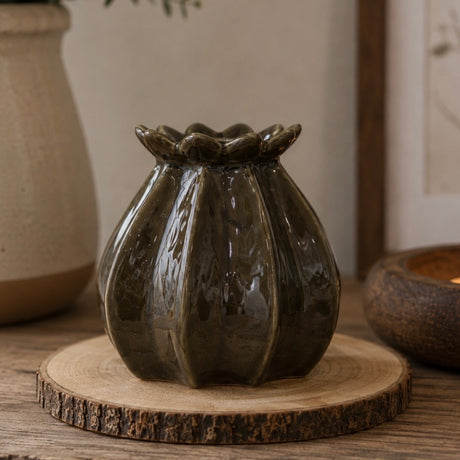 A glossy dark green ceramic bud vase in a poppy bud shape, displayed on a rustic round wood slice coaster.