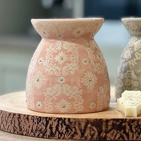 Decorative pink ceramic oil burner with floral patterns on a wooden surface.