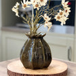 Decorative vase with white flowers on a wooden stand in a kitchen setting