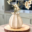 White ceramic vase with flowers on a wooden stand in a kitchen setting