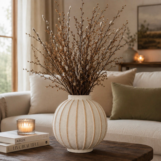 A ribbed cream ceramic vase filled with dried willow branches, styled on a dark wood coffee table in a cozy living room setting.
