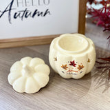 Ceramic pumpkin Wax Burner with 'Autumn Magic' text, placed on a wooden surface and a framed 'Hello Autumn' sign in the background