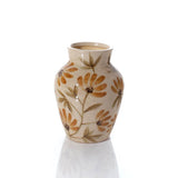 A small ceramic vase with a cream-colored glaze, decorated with a pattern of orange-brown daisy-like flowers and olive-green leaves, shown on a reflective white surface against a white background.