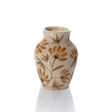 A small ceramic vase with a cream-colored glaze, decorated with a pattern of orange-brown daisy-like flowers and olive-green leaves, shown on a reflective white surface against a white background.