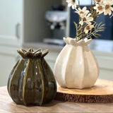Two ceramic vases, one dark green and one white, on a wooden surface with a blurred background.