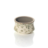 A small round ceramic planter with a green floral pattern and a beige rim, shown on a reflective white surface against a white background