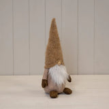 Stuffed gonk with a tall brown hat on a light wooden surface with a neutral background