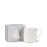 White mug with pink heart patterns in a branded box on a white background