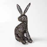A rustic woven wire haresculpture in a sitting position, crafted from dark brown and black recycled wire, set against a plain white studio background.