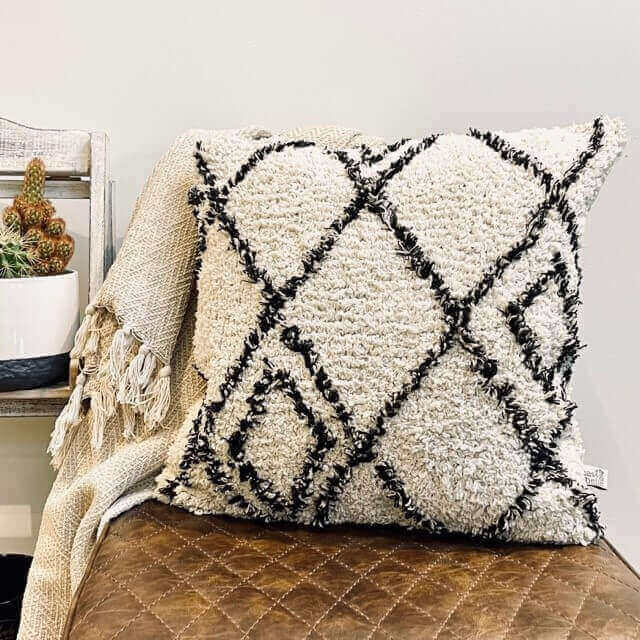 A cream and black berber style scatter cushion placed on a kitchen bar stool and a throw draped over the side
